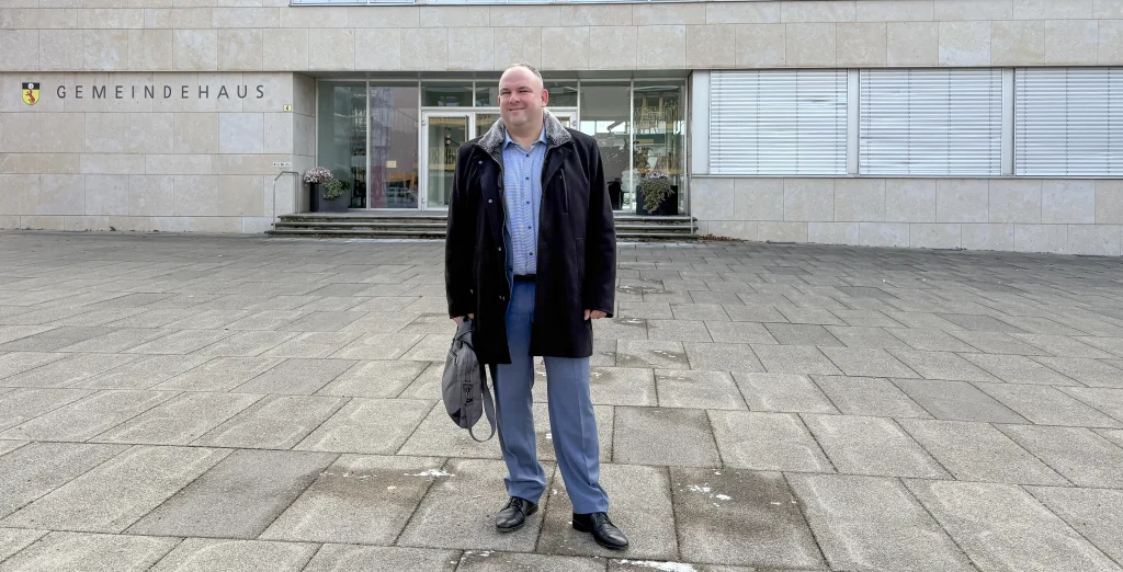 Daniel Wäfler steht mit einem Aktenkoffer vor der Gemeindeverwaltung Gossau ZH. Zurzeit kandidiert er als Gemeindepräsident bei den Kommunalen Wahlen 2026.