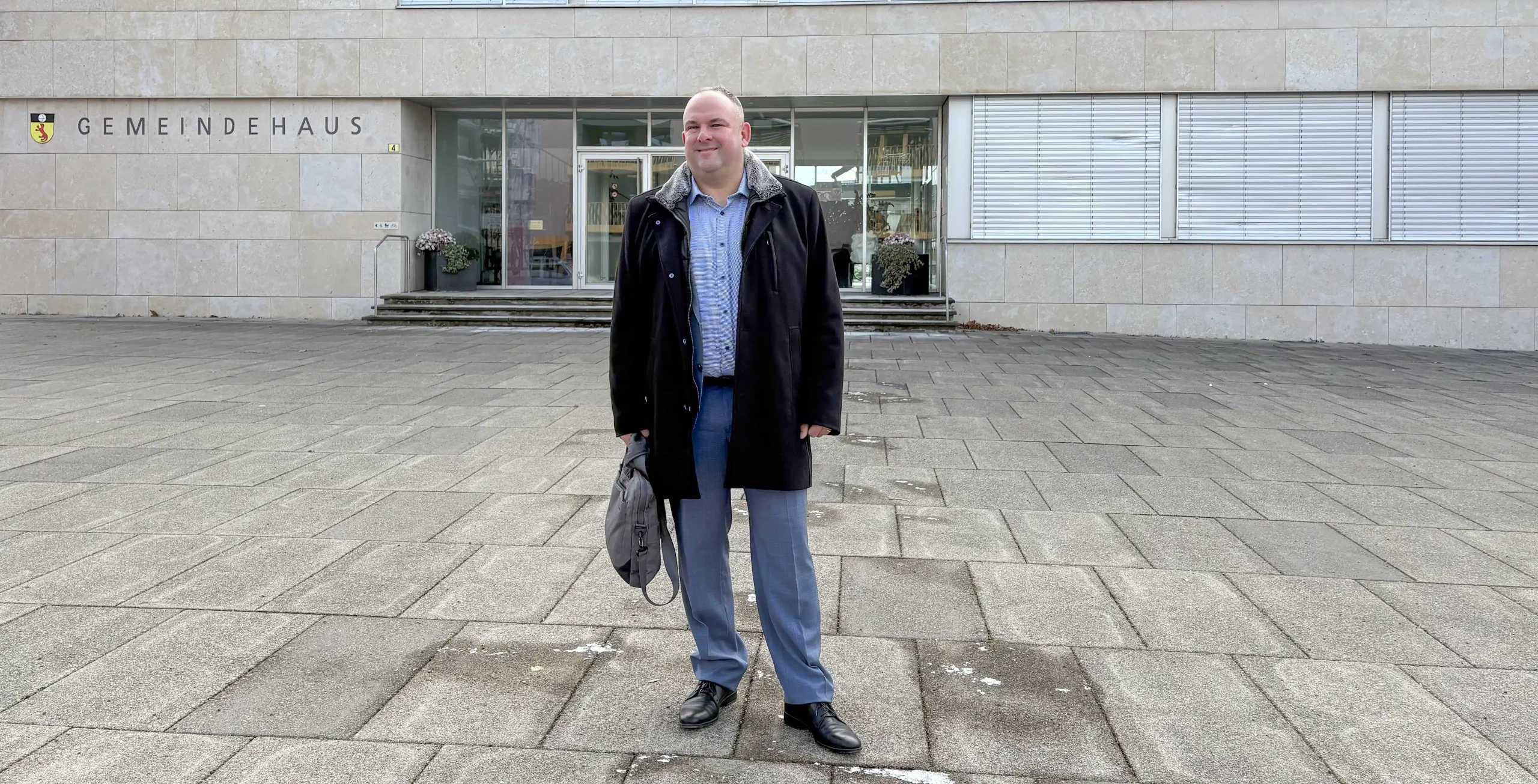 Daniel Wäfler steht mit einem Aktenkoffer vor der Gemeindeverwaltung Gossau ZH. Zurzeit kandidiert er als Gemeindepräsident bei den Kommunalen Wahlen 2026.