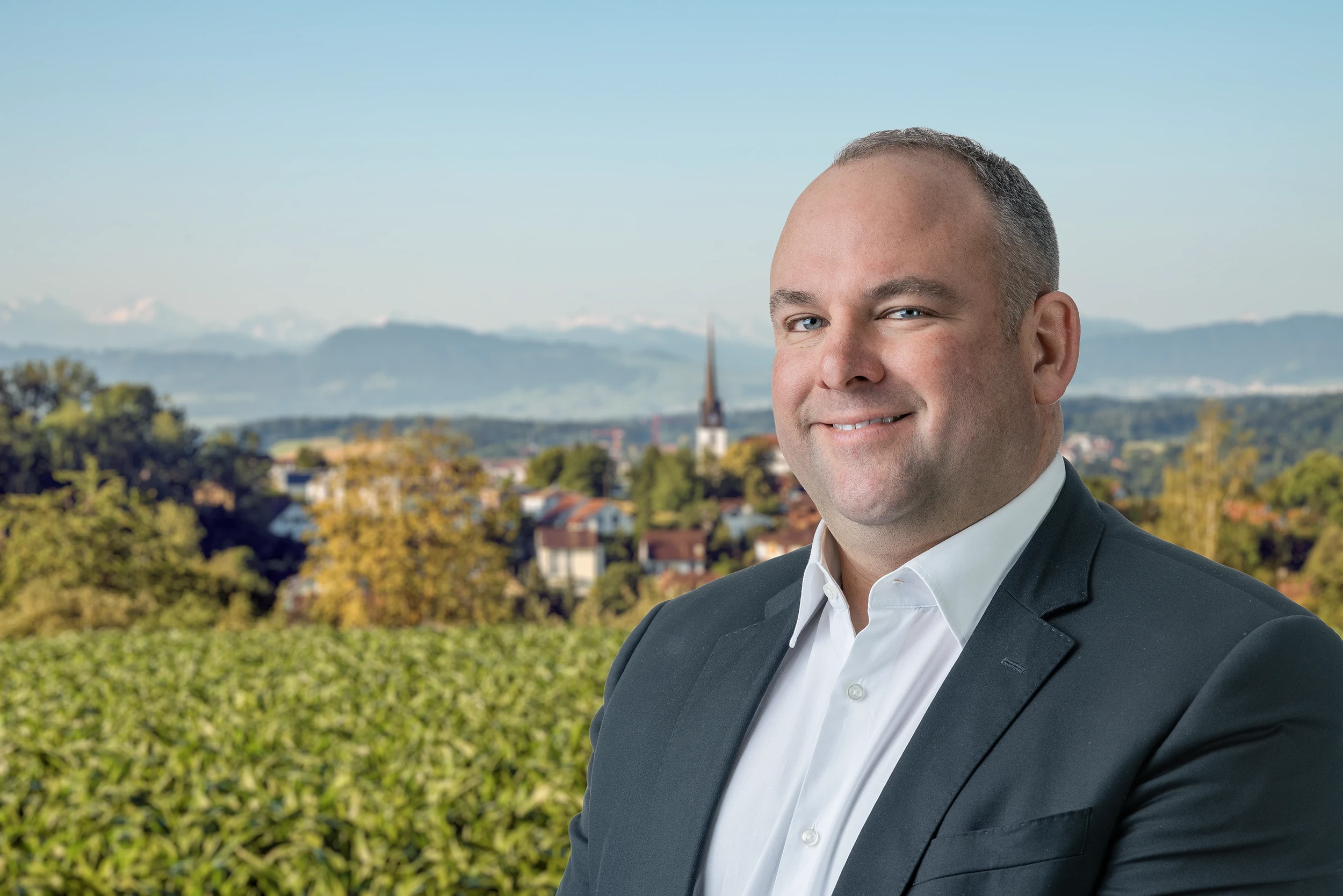 Ein Portraitbild von Daniel Wäfler aus Gossau ZH. Man sieht den Politiker und dahinter die Gemeinde Gossau ZH. Der Kantonsrat kandidiert bei den Gemeindewahlen 2026 in Gossau ZH.